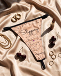 The She. Slippery When Wet thong styled flat on champagne satin with gold hoops, chains, rings, lipstick and cherries
