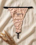Flat lay of the She. Slippery When Wet thong showing the full doodle print and black trim